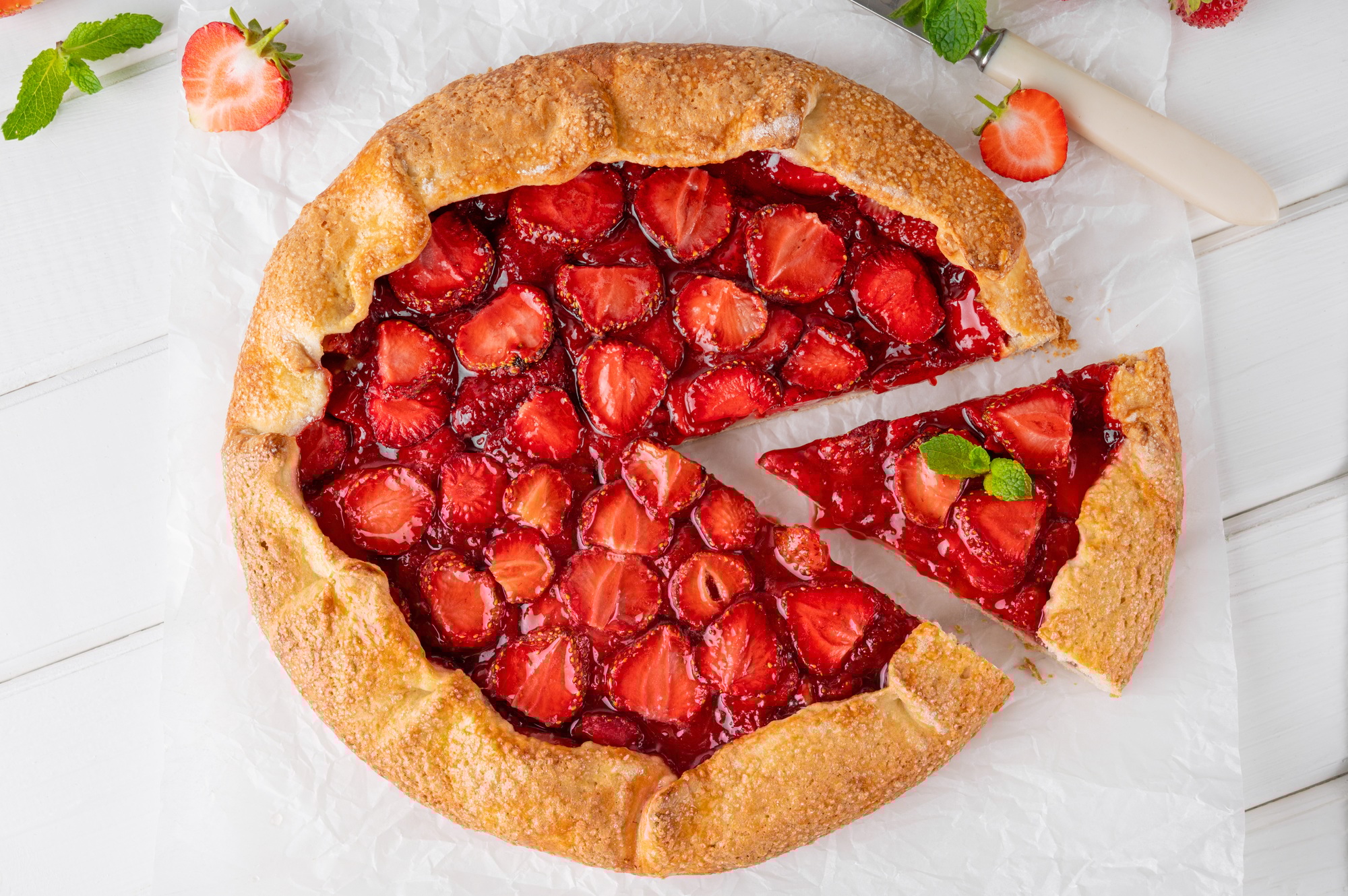 Galette, open pie or tart with strawberries with cup of tea on a white wooden table