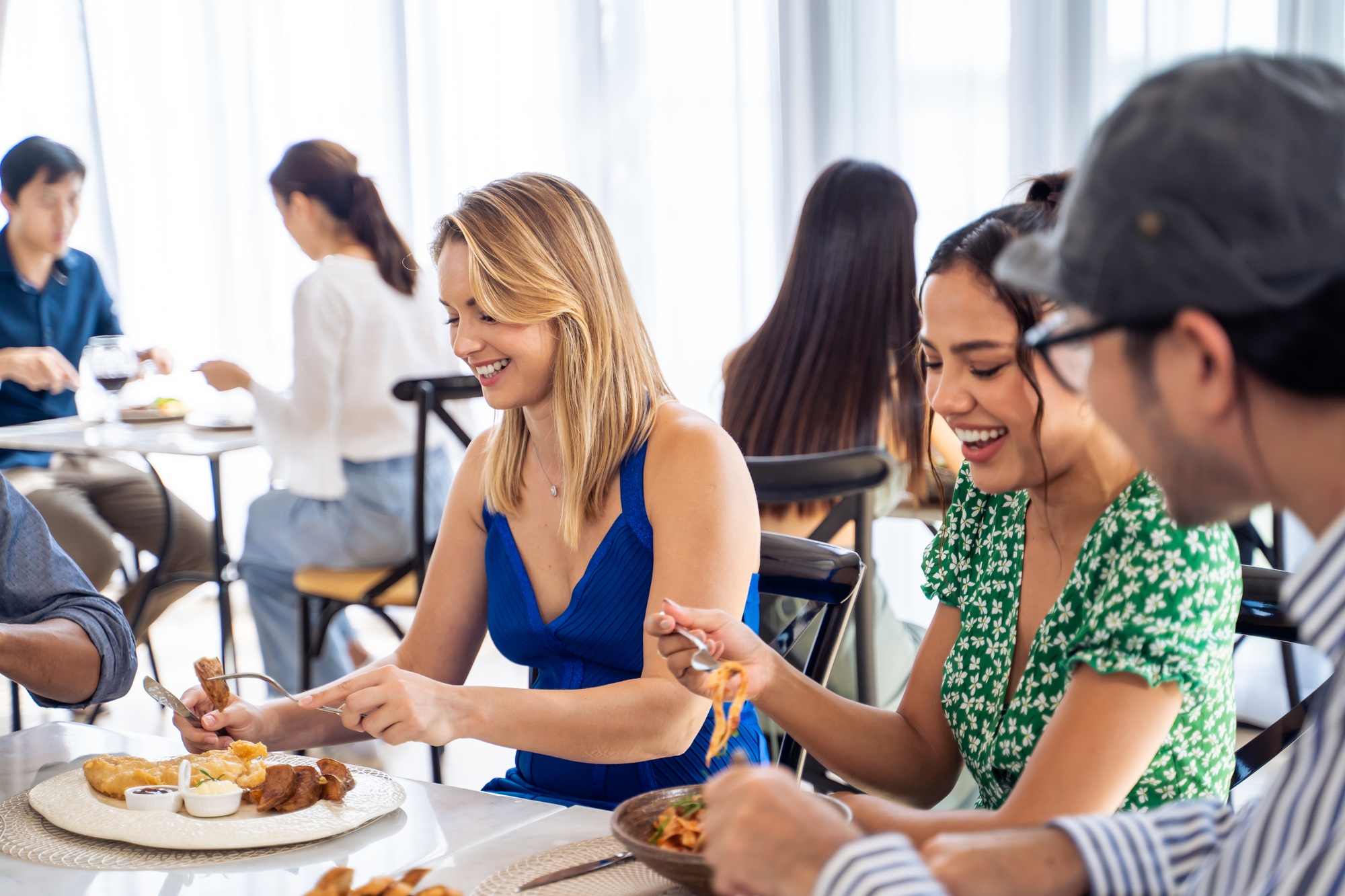 Group of diverse friend talking and eating food together in restaurant.