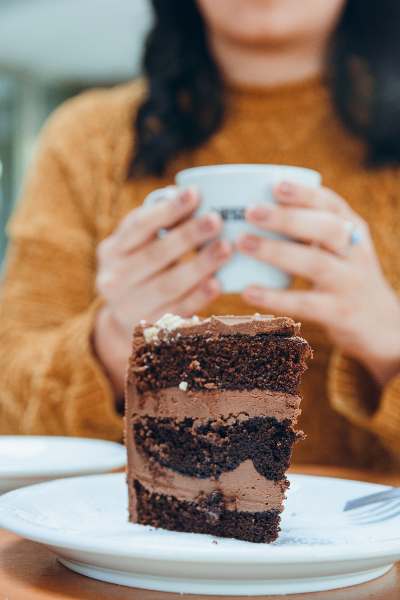portion of chocolate cake with unrecognizable blurred woman drinking coffee at le fondo